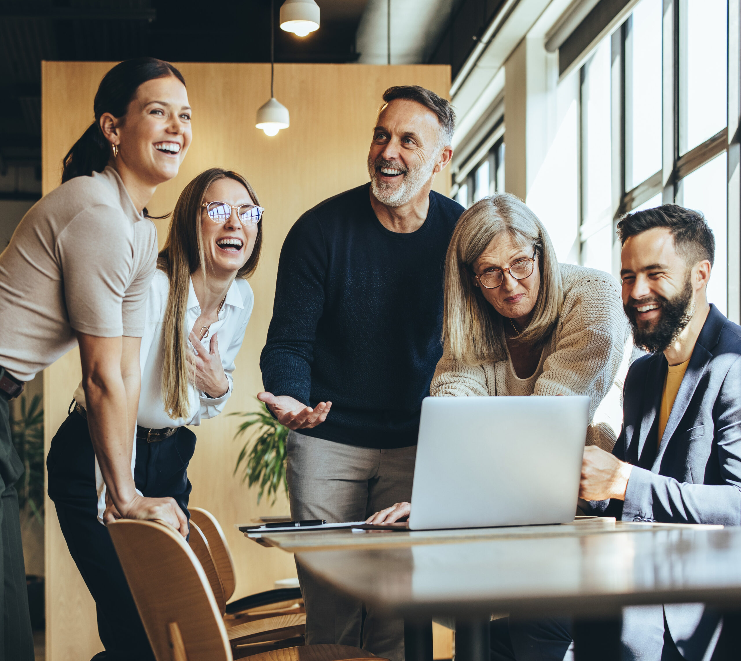 Five professional individuals engaged in work and laughter around a computer